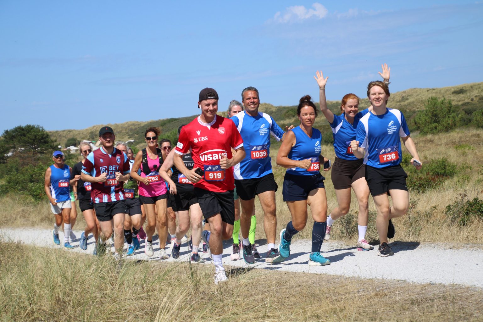 Groep hardlopers met startnummers op een duinpad tijdens de halve marathon van Vlieland
